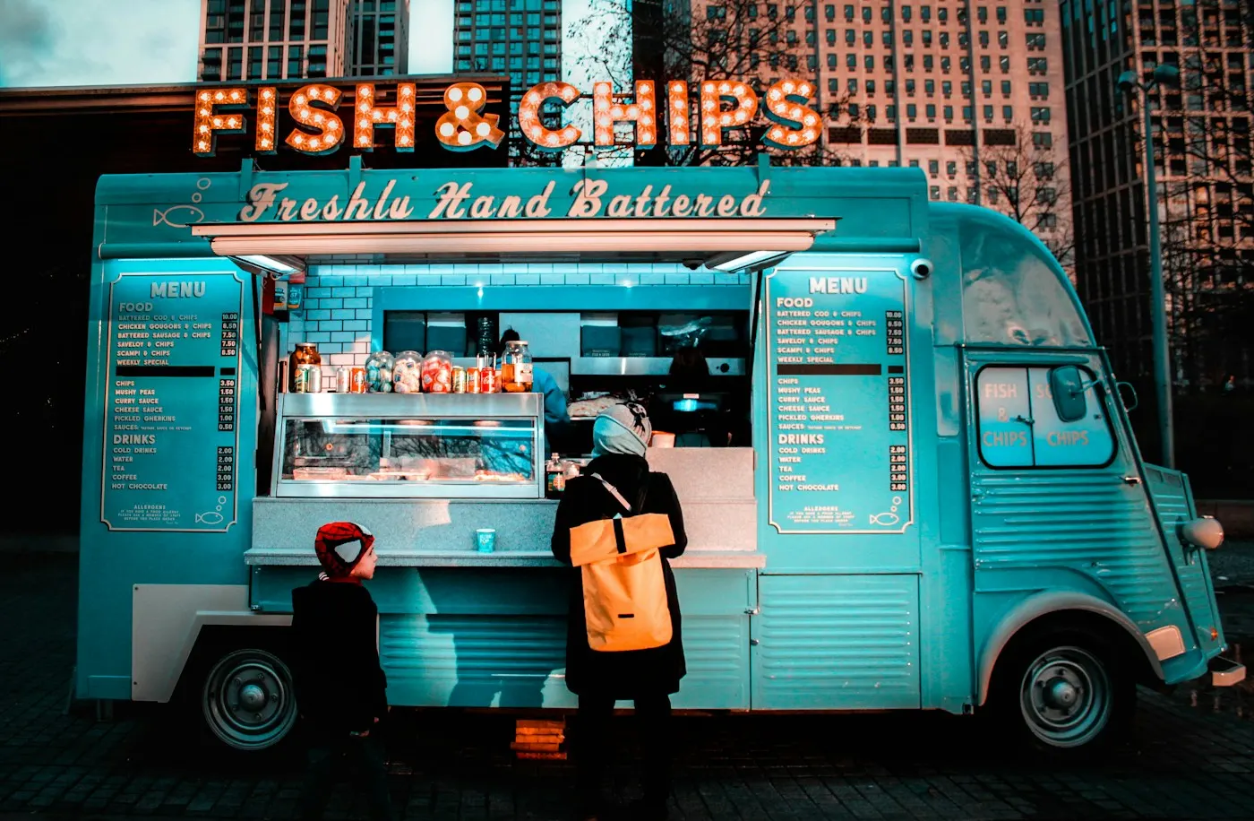 Un food truck turquoise servant des clients sur une place.