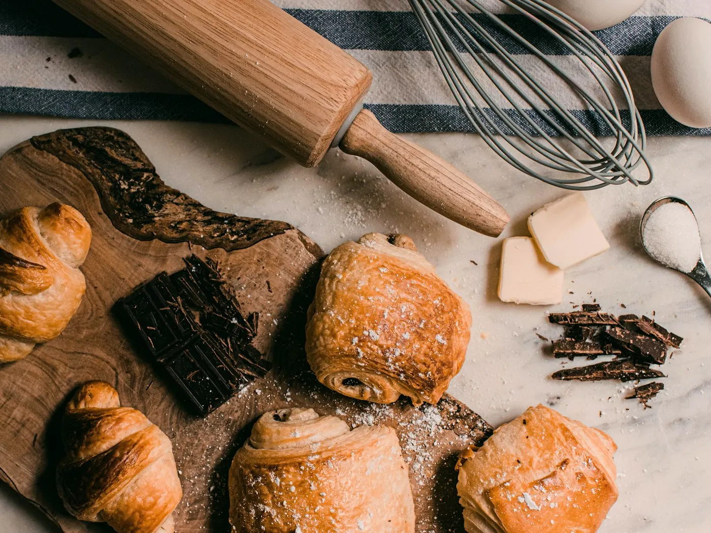 Croissants et pains au chocolat sur une planche, rouleau à pâtisserie.