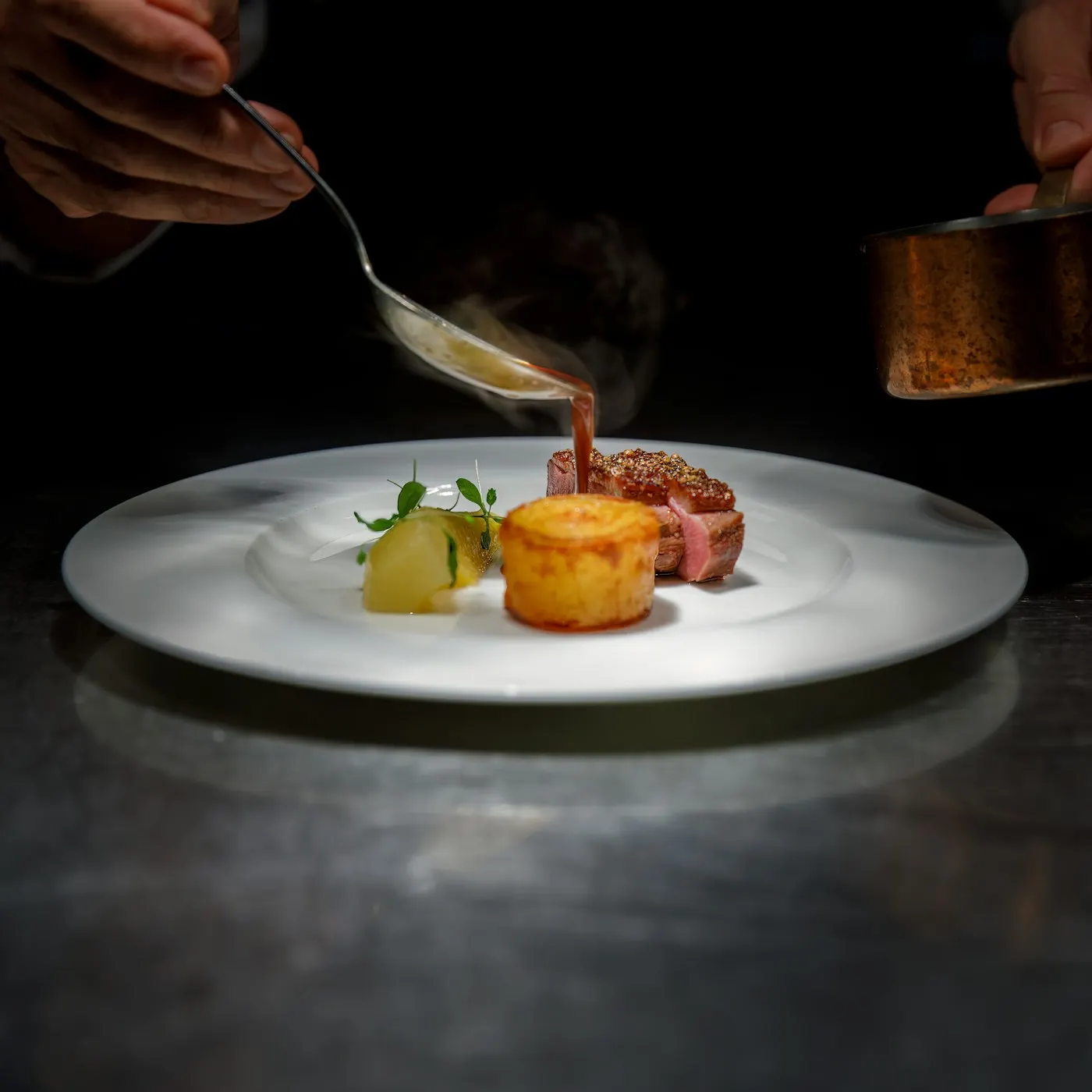 Un chef nappe de sauce une assiette dressée.